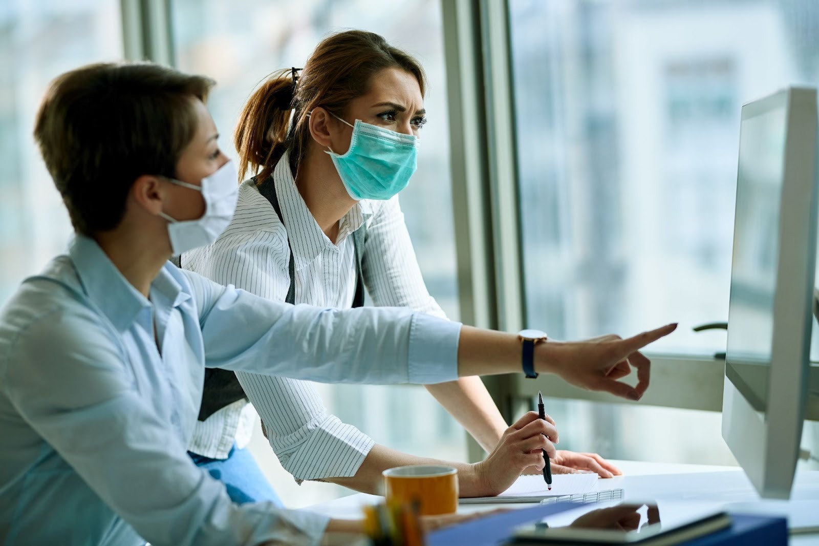 young businesswoman and her colleague wearing face masks while working on a computer in an office during a virus epidemic